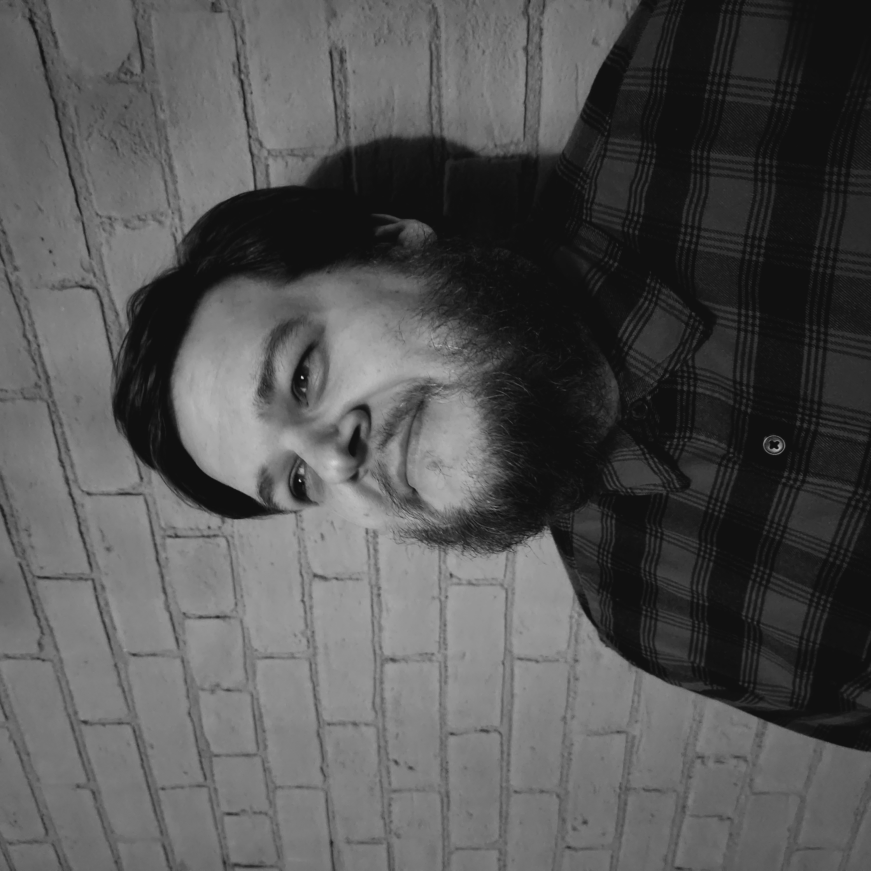 Headshot of Andrew Wood, a bearded individual against a brick wall