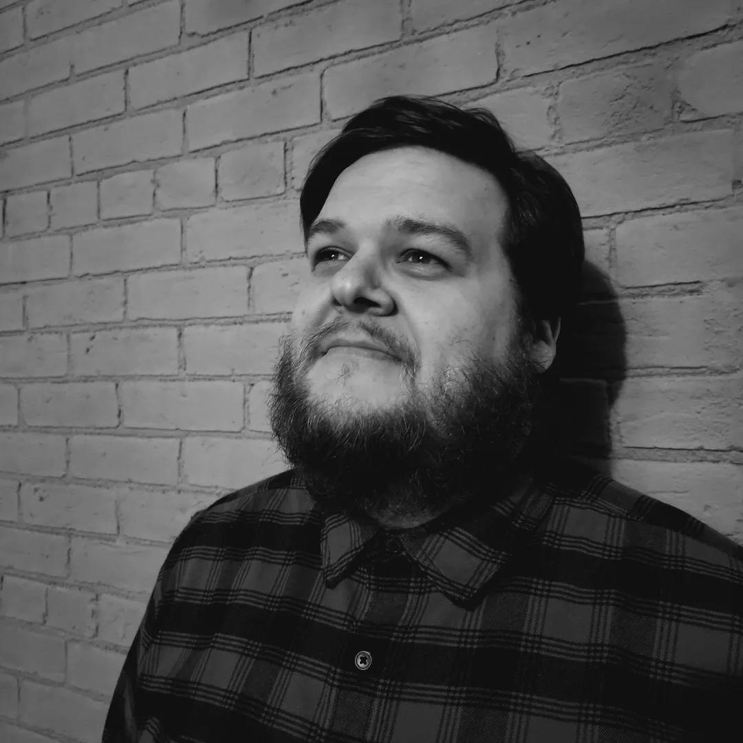 Headshot of Andrew Wood, a bearded individual against a brick wall
